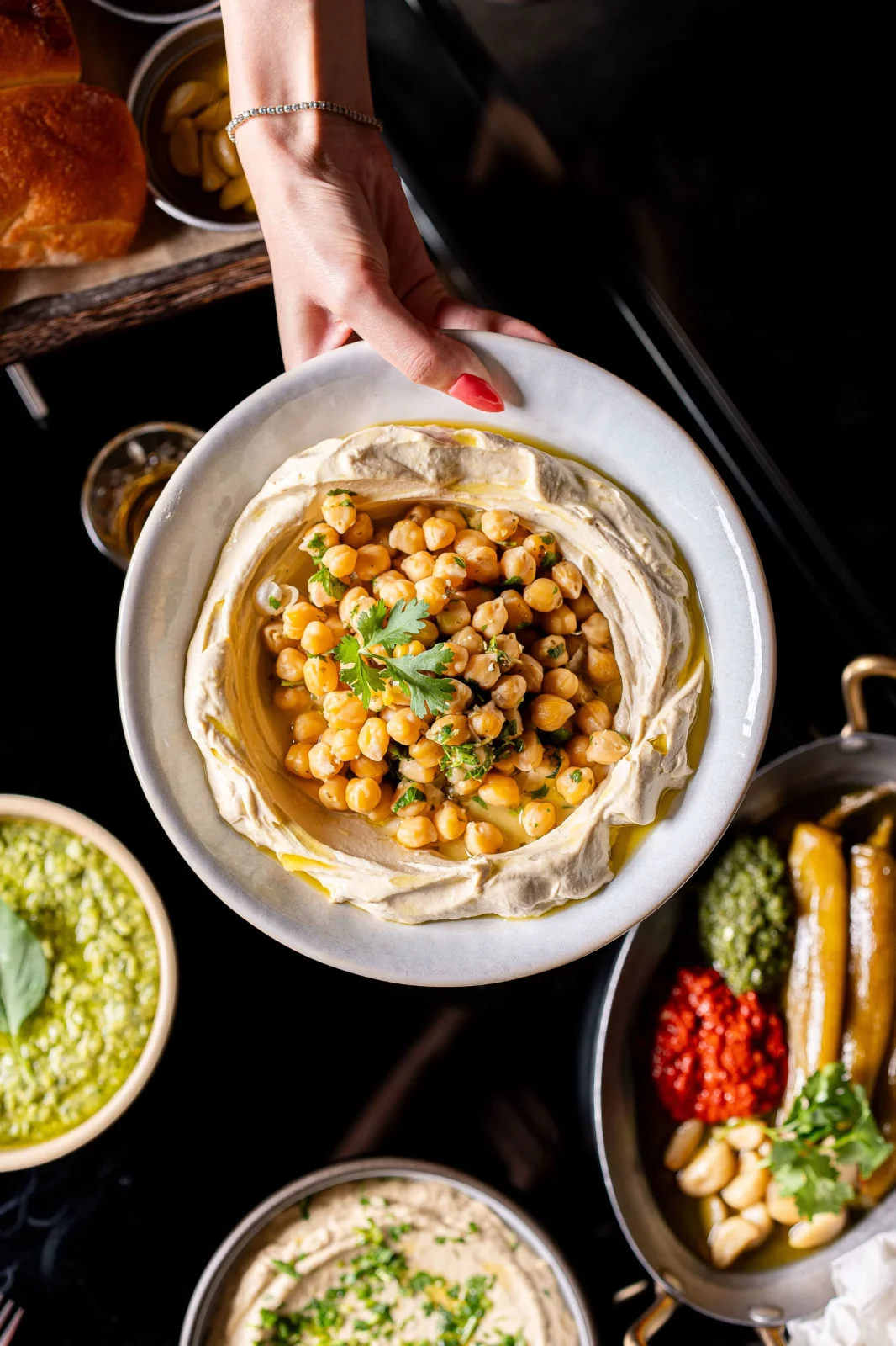 צלחת חומוס עם גרגרי חומוס ושמן זית, מוגשת עם רטבים נוספים. אידיאלי לאירועים קטנים.