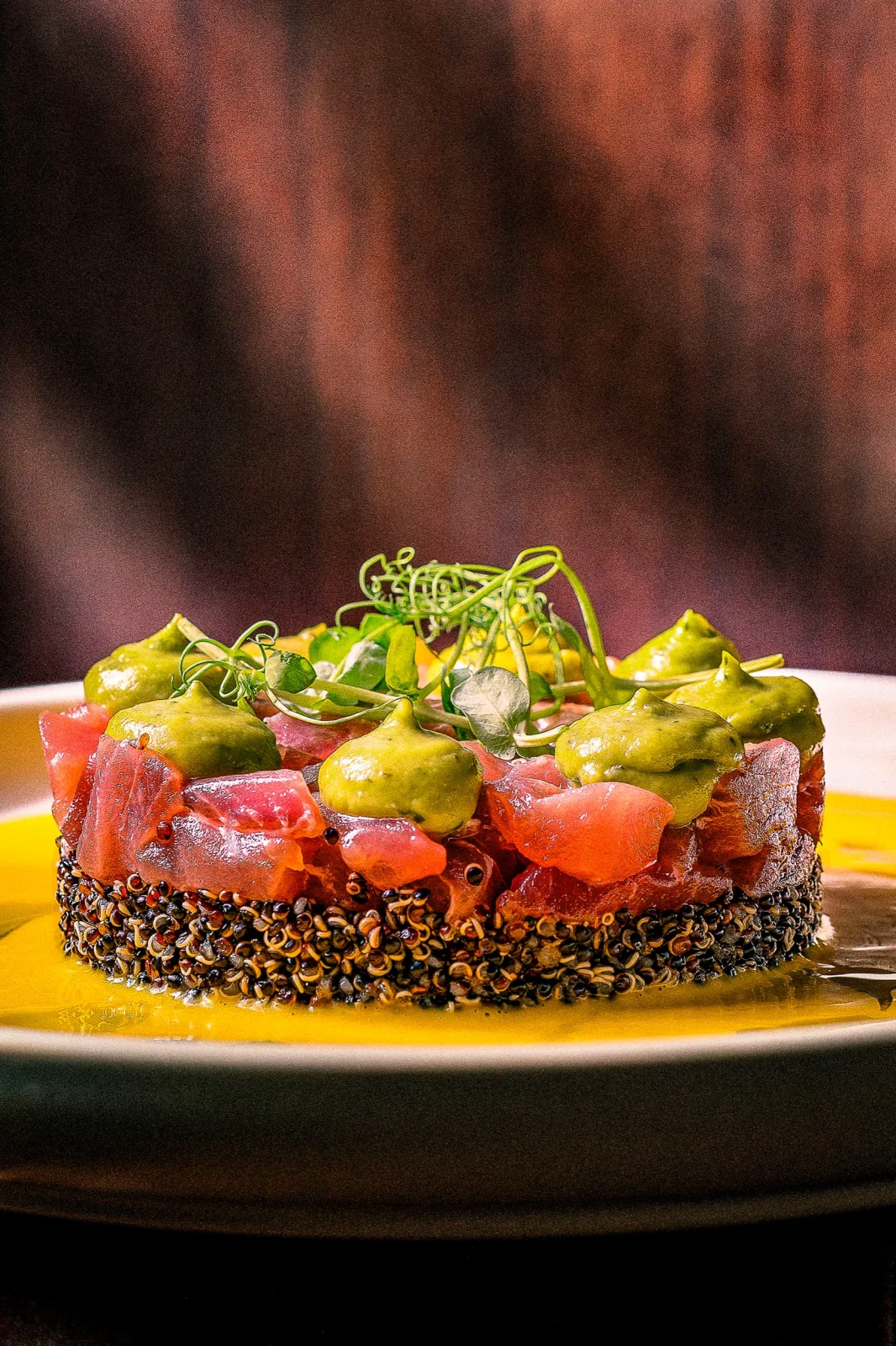 מנה מעוצבת של טונה עם אבוקדו על שכבת קינואה, מוגשת בצלחת עגולה עם רוטב צהוב.