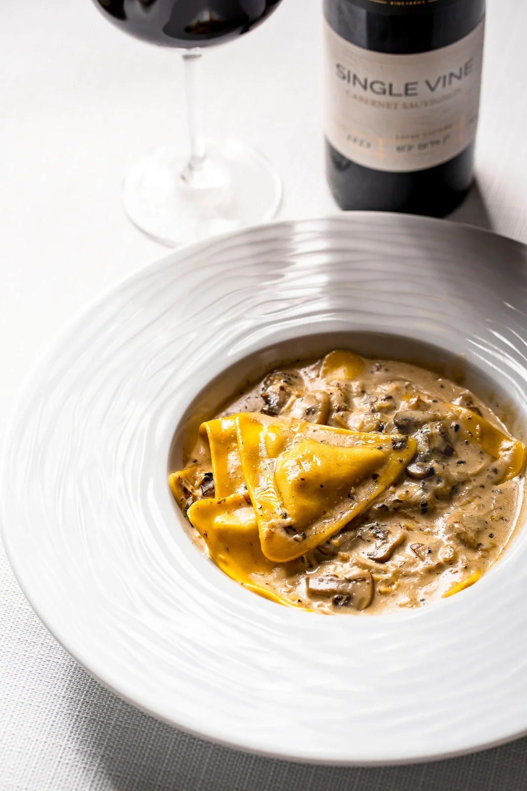 מנה של פסטה רטובה ברוטב שמנת עם פטריות, בקבוק יין אדום וכוס יין.