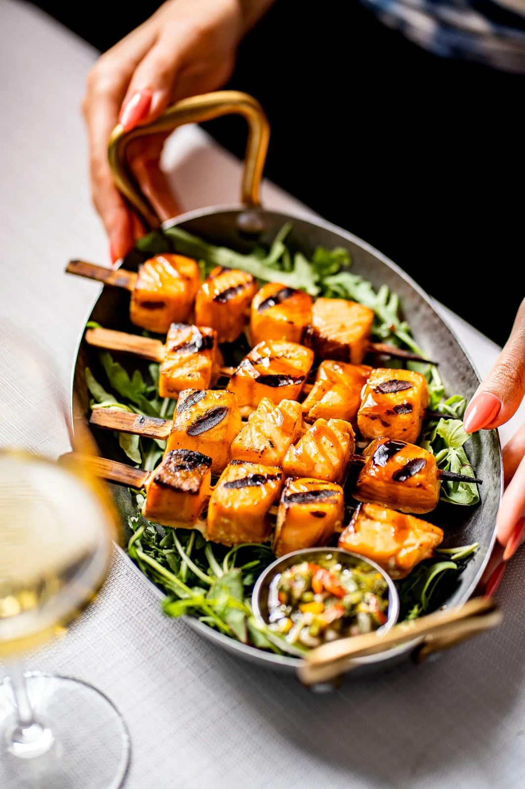 שיפודי סלמון על רוקט, מוגשים בכלי מתכת עם רוטב בעבודת יד, מושלם לאירועים קטנים.