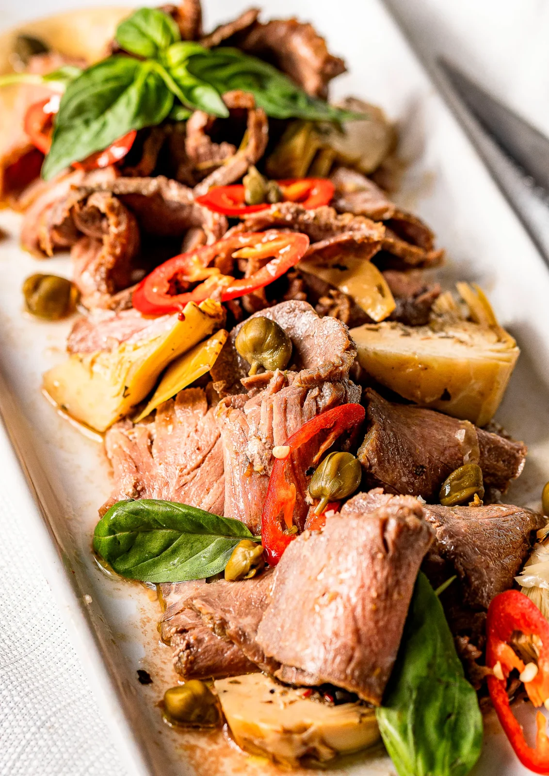 צלחת עם נתחי בשר רך, פרוסות ירקות, בזיליקום ופלפל חריף, מוגשת על רקע לבן.